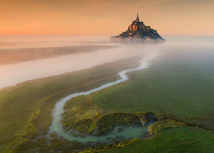 Aerial view to castle Mont Saint-Michel in orange sunset in France